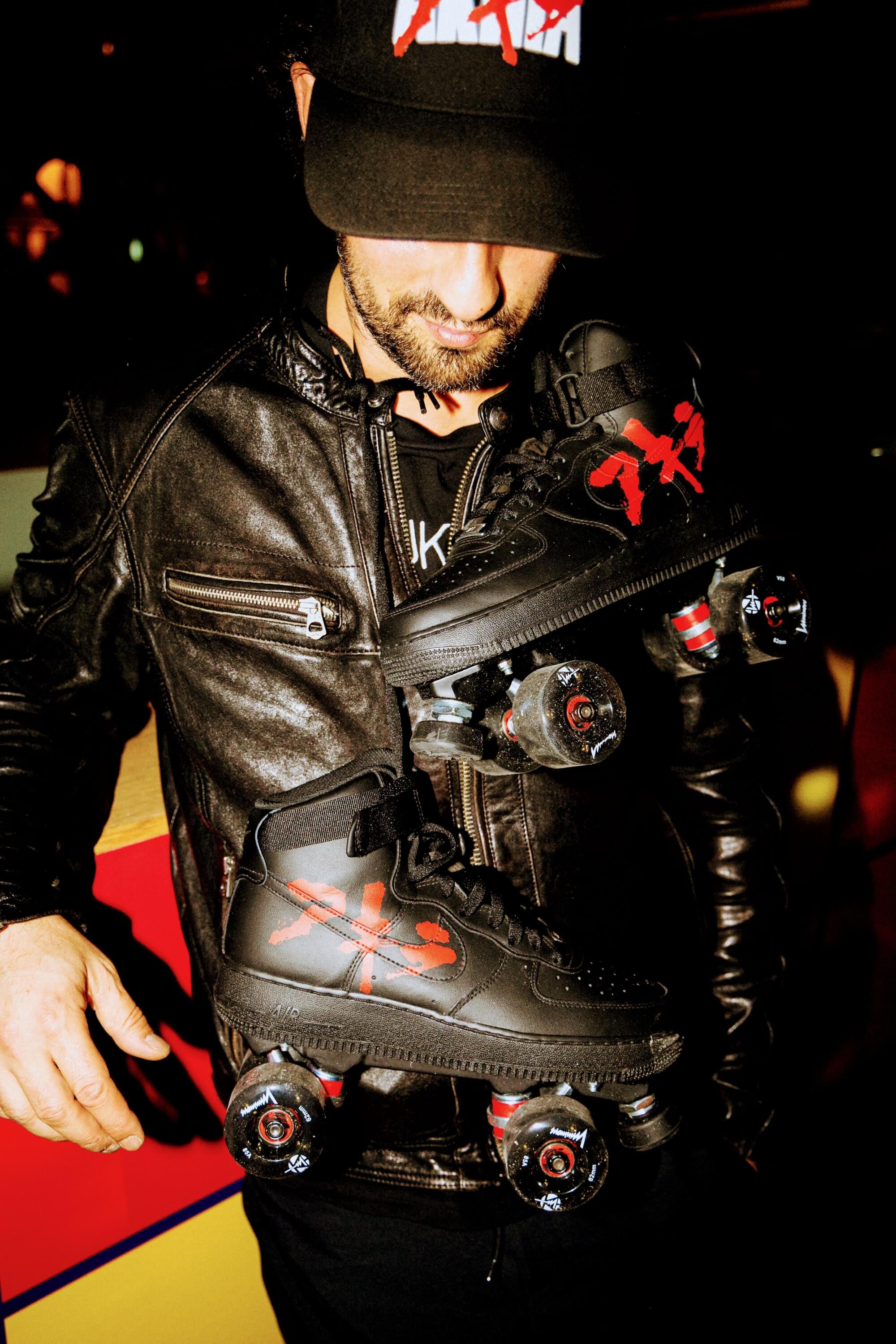 LOUMY wearing a black leather jacket and Akira cap with red lettering, holding his custom Akira roller sneakers by LOUMY x KAZY around his neck