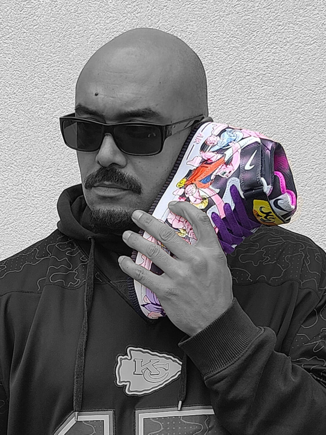 Black-and-white portrait of Kazy in sunglasses holding a Nike Air Force 1 Mid he hand-painted with Majin Buu from Dragon Ball Z for Loumy’s World