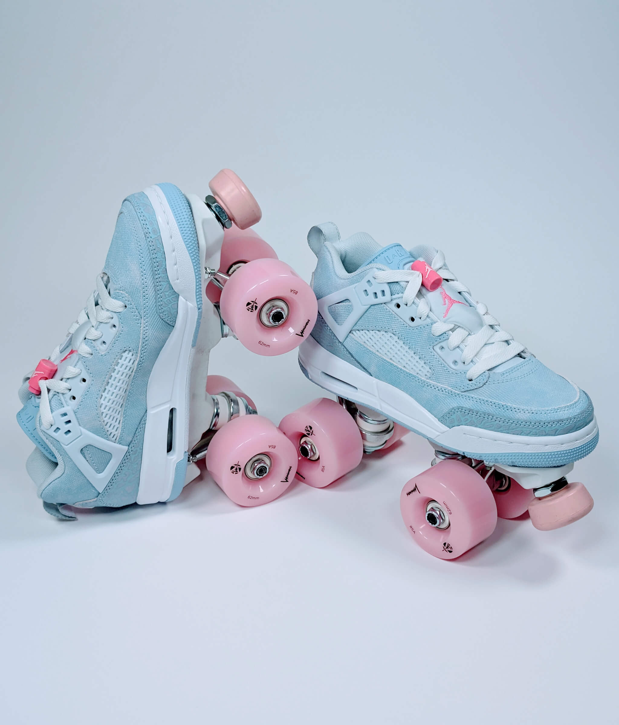 Loumy's Nike Jordan Spizike roller sneakers in blue and pink, one flat and one standing on the heel in side-by-side view, with pink luminous wheels